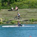 young man rowing kayak in foreground with gentleman on bike taking video in background