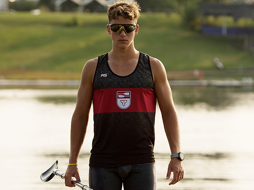 young man in black tank top with red stripe lake shore in background