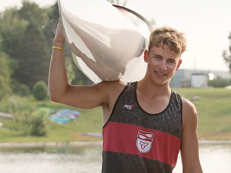 young man in tank top with red stripe holding kayak on right shoulder