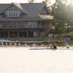 young man paddling in kayak with yach club building in background