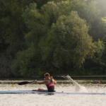 young man paddling in kayak with trees in background