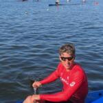 young man in red and black sports outfit sitting in a kayak on a lake