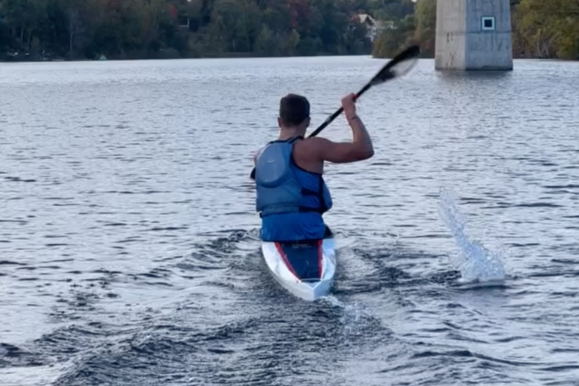 view from directly behind young man rowing in kayak approaching bridge