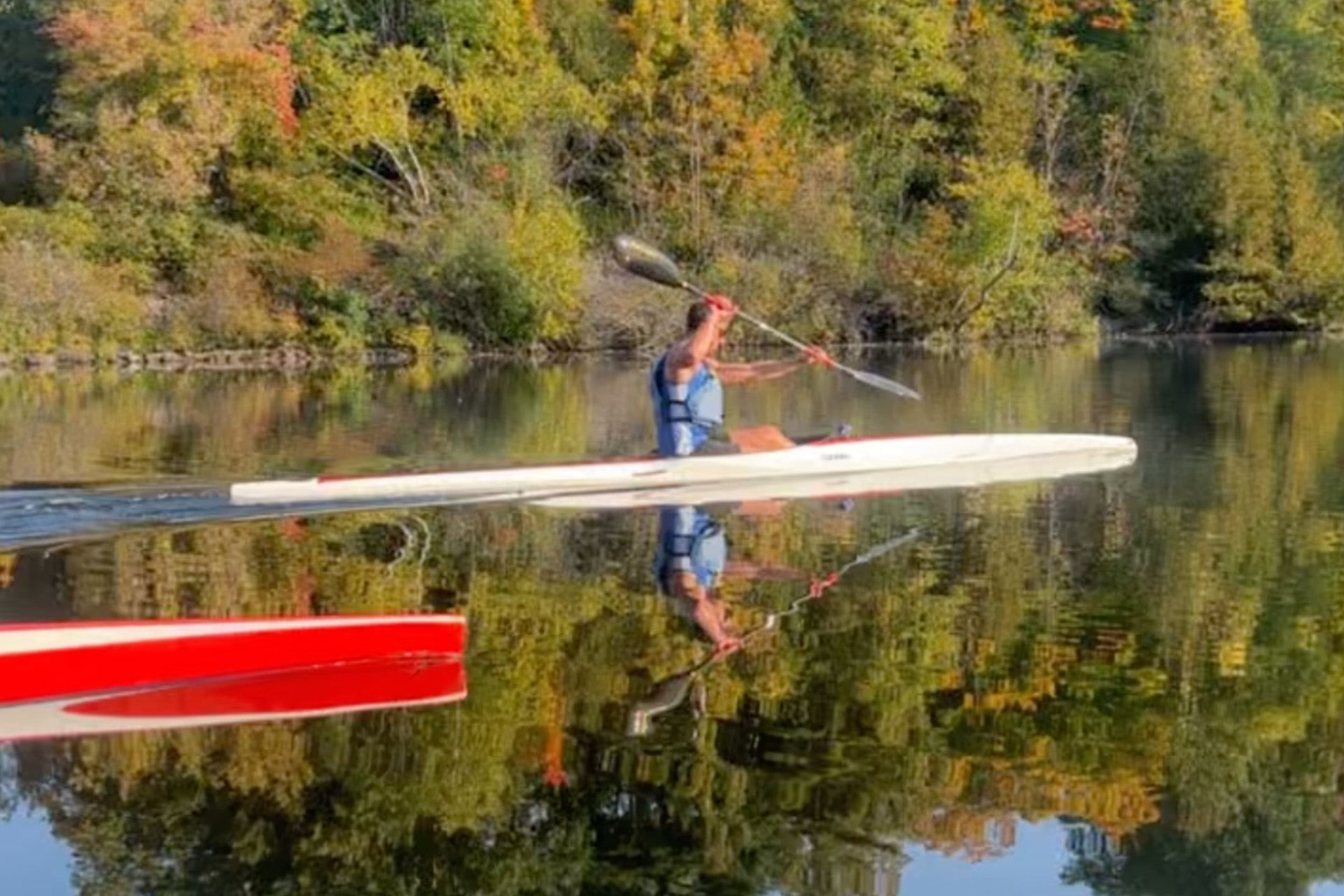 young man rowing in kayak on lake with autumn trees in background